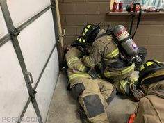 two firemen in protective gear laying on the ground next to a garage door,