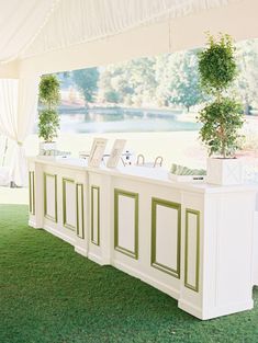 a row of white tables sitting on top of a green grass covered field under a tent