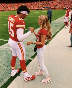 a man in a football uniform talking to a woman on the sidelines at a stadium