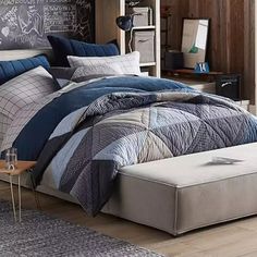 a bed with blue and grey comforters in a room next to a chalkboard