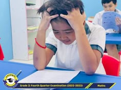 a young boy sitting at a table with his head in his hands and reading a book