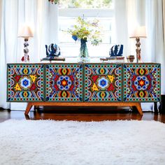 an ornately decorated sideboard in front of a window with two lamps on each side