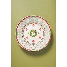 a white plate with red and green designs hanging on the wall next to a green wall