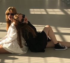 two beautiful young women sitting on the ground next to each other with their legs crossed