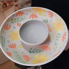 a person holding a large white bowl with flowers painted on the bottom and inside it