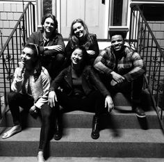 five people sitting on the steps in front of a door and smiling at the camera