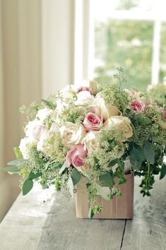 a vase filled with white and pink flowers sitting on top of a wooden table next to a window