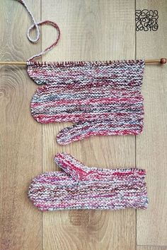 two knitted mittens sitting on top of a wooden floor next to a knitting needle