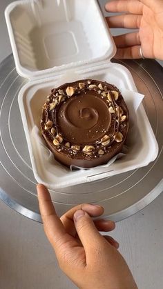 someone is holding a container with a chocolate cake in it