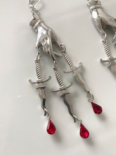 Bring a touch of the macabre to your next outfit with these elegant, yet ominous, earrings. With highly detailed designs available in either gold or silver finish, and red crystal drops suspended below, these earrings will ensure you stand out from the crowd. A great choice for fashion forward ladies with a dark taste. Dagger Earrings, Backpack Lunch Bag, Gothic Earrings, Candle Wax Melts, Jewelry Pins, Red Crystals, Crystal Drop, Earring Necklace, The Golden