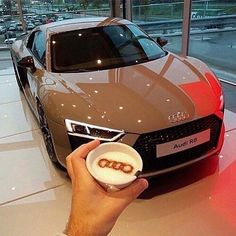 a hand holding a small plate with some food in front of a parked audi car