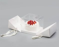 a white cake with strawberries on top in a clear box next to a measuring tape