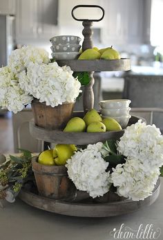 a three tiered tray filled with white flowers and apples on top of a table