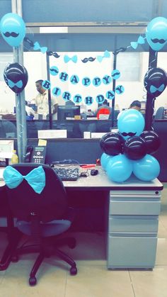 an office cubicle decorated with blue balloons and black bow ties for the birthday boy