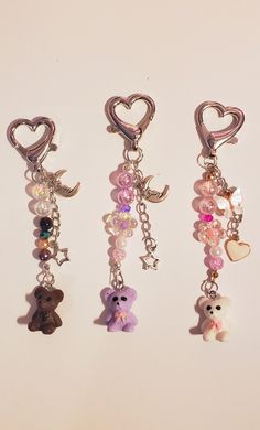 three key chains with different charms attached to them, one has a teddy bear and the other has a heart