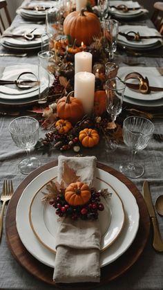 the table is set for thanksgiving dinner with candles and pumpkins on it, along with other place settings