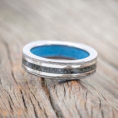 a wedding band with blue inlays sits on top of a piece of wood