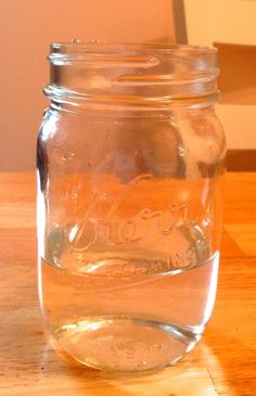 a glass jar filled with water sitting on top of a wooden table next to a wall