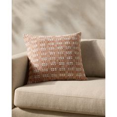 an orange and white pillow sitting on top of a couch next to a plant in a vase