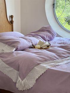 an open book laying on top of a purple comforter in a bedroom with a round window