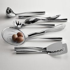 silverware and utensils are arranged on a white surface with an egg in the middle