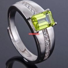 an image of a ring with a green stone and diamonds on the sides, set in white gold