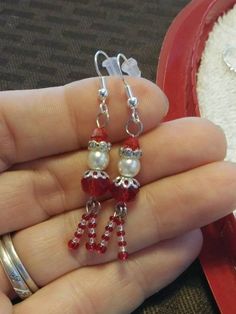 a pair of red and white beaded earrings in someone's hand next to some jewelry