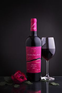 a bottle of wine sitting next to a glass filled with red wine and a rose