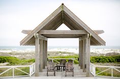 a gazebo sitting on top of a wooden deck next to the ocean with chairs around it