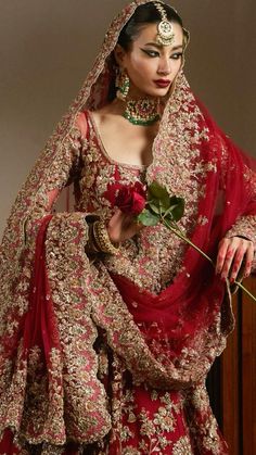 a woman in a red and gold bridal gown holding a rose with her right hand