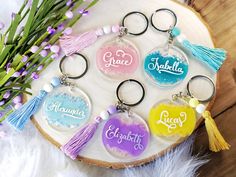 six personalized keychains with tassels are arranged on a piece of wood