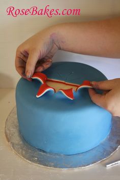 a person is decorating a blue cake with red and white icing on it