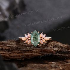 a ring with an emerald stone surrounded by pink and white flowers on top of a piece of wood