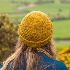 a woman with long hair wearing a yellow knitted hat looking out over the countryside