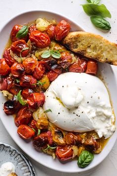 a white plate topped with an egg and tomato salad next to bread on a table