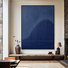 a large blue painting hangs on the wall above a bench in a living room with stone fireplace