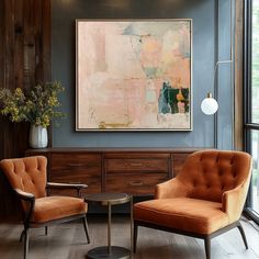 two orange chairs sitting in front of a painting on the wall next to a coffee table