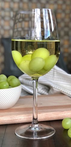 a wine glass filled with green grapes on top of a wooden table