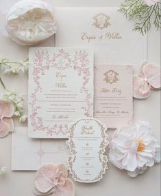 the wedding stationery is laid out with pink flowers and greenery on top of it