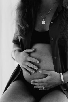 black and white photograph of a pregnant woman with her hands on her stomach, looking at the camera