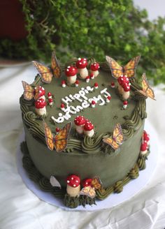 a green birthday cake with butterflies and mushrooms on it's top is sitting on a white tablecloth