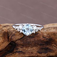 an aqua blue topazte and diamond ring sitting on a piece of driftwood