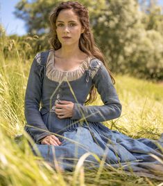 a woman sitting in tall grass wearing a blue dress