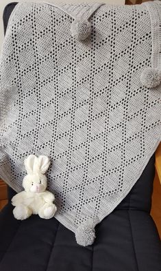 a white stuffed animal sitting on top of a black chair next to a gray blanket