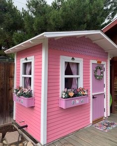 a small pink house with two windows and flower boxes on the front window sill