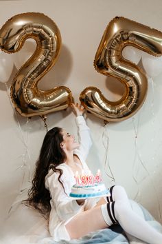 a woman sitting on the floor with balloons and a cake