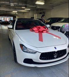 a white car with a red bow on it's hood in a parking garage