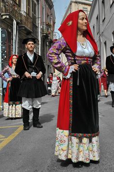 some people are dressed in traditional clothing and walking down the street with one woman wearing a red headdress