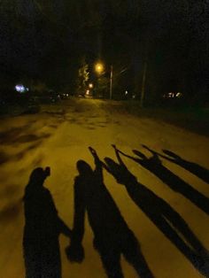 several people standing in the street at night with their shadows on the ground and one person holding his hand