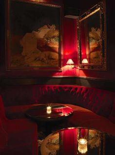 a red couch sitting next to a table with candles on top of it in front of two framed pictures